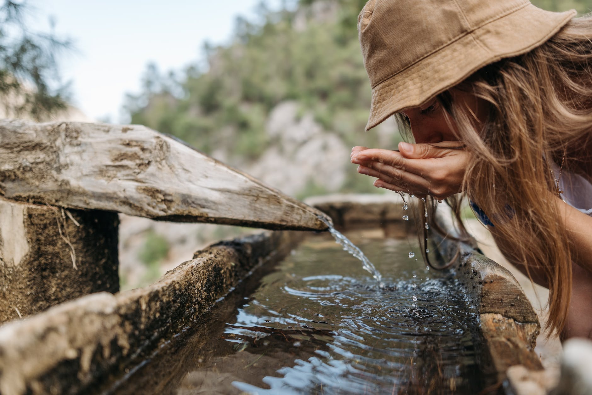 woman in brown hat drinking water from a fountain